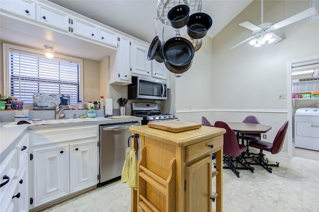 kitchen with appliances with stainless steel finishes, washer / clothes dryer, white cabinetry, sink, and ceiling fan