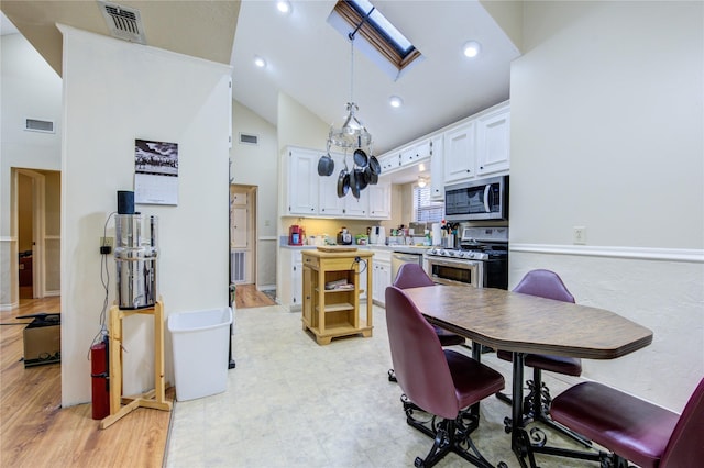 kitchen with appliances with stainless steel finishes, white cabinetry, hanging light fixtures, a skylight, and high vaulted ceiling