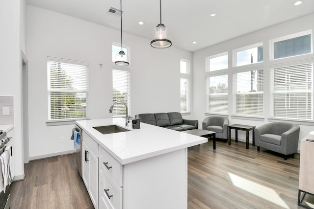 kitchen with a kitchen island with sink, sink, hanging light fixtures, hardwood / wood-style flooring, and white cabinetry