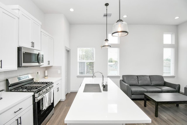 kitchen featuring white cabinetry, sink, hanging light fixtures, a kitchen island with sink, and appliances with stainless steel finishes