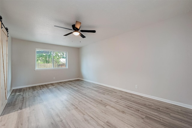 empty room with ceiling fan, a barn door, light hardwood / wood-style floors, and a textured ceiling