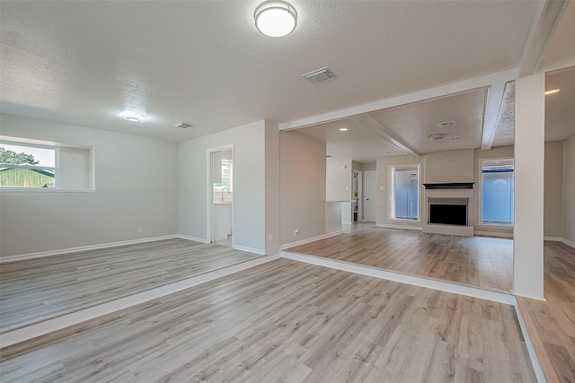 unfurnished living room with a fireplace, a textured ceiling, and light hardwood / wood-style floors