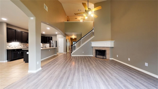 unfurnished living room featuring ceiling fan, a fireplace, high vaulted ceiling, and light hardwood / wood-style flooring