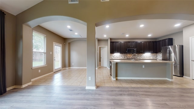 kitchen with backsplash, a center island with sink, appliances with stainless steel finishes, dark brown cabinets, and light hardwood / wood-style floors