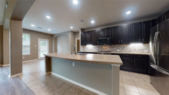 kitchen featuring backsplash, stainless steel appliances, sink, light tile patterned floors, and an island with sink