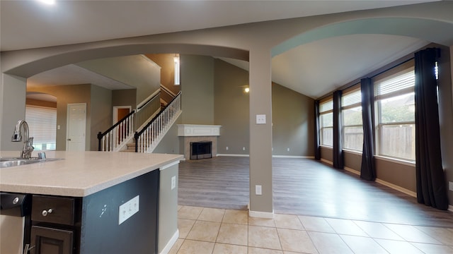 kitchen featuring a center island with sink, sink, stainless steel dishwasher, light tile patterned flooring, and a tiled fireplace