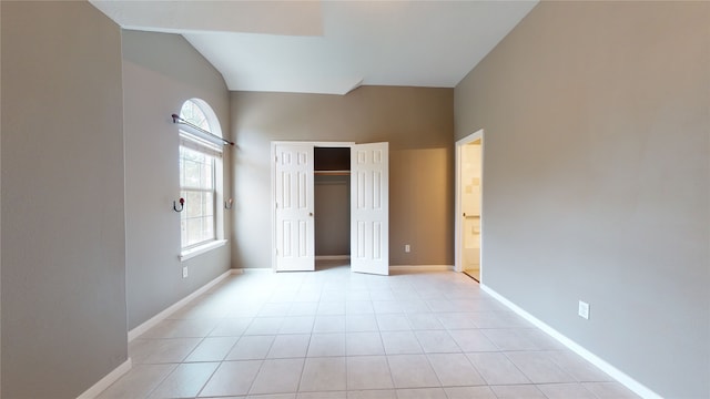 unfurnished bedroom with a closet, light tile patterned floors, and vaulted ceiling