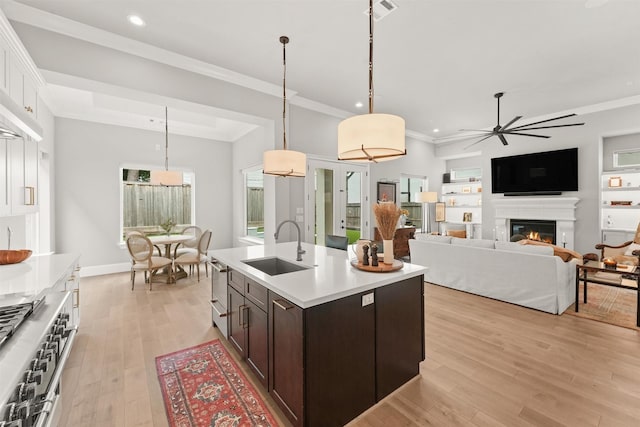 kitchen featuring dark brown cabinetry, sink, light hardwood / wood-style flooring, pendant lighting, and a center island with sink