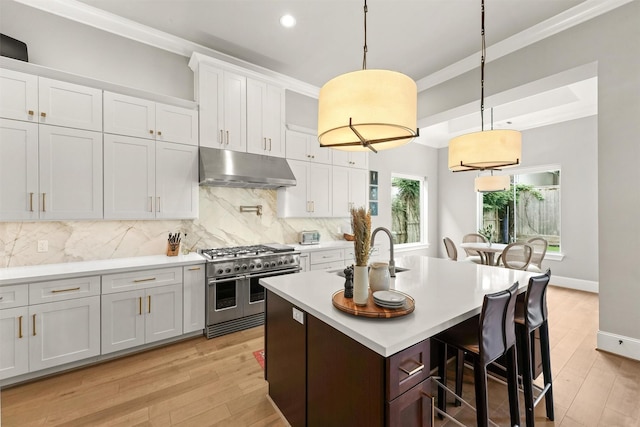 kitchen featuring backsplash, range with two ovens, white cabinets, hanging light fixtures, and an island with sink