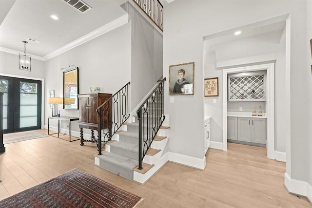 entryway featuring french doors, an inviting chandelier, light hardwood / wood-style flooring, and crown molding