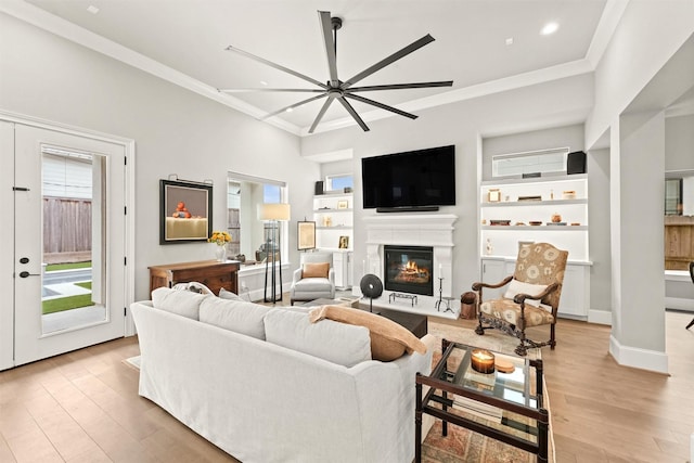 living room featuring built in features, light hardwood / wood-style flooring, ceiling fan, and crown molding