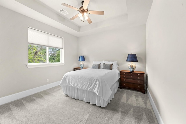 carpeted bedroom with a raised ceiling and ceiling fan