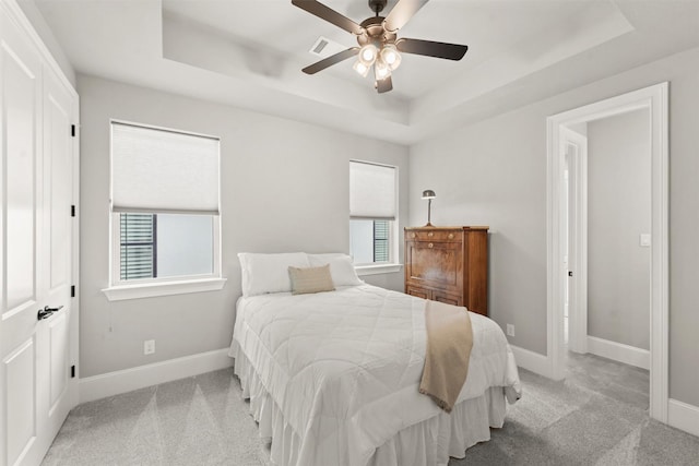 bedroom with ceiling fan, a raised ceiling, and light colored carpet