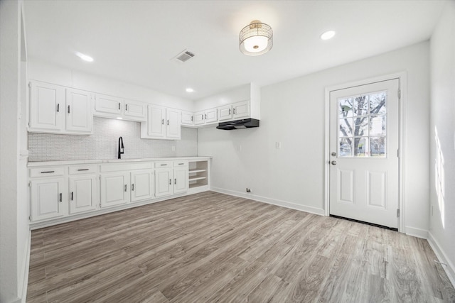 interior space with white cabinets, decorative backsplash, light wood-type flooring, and sink