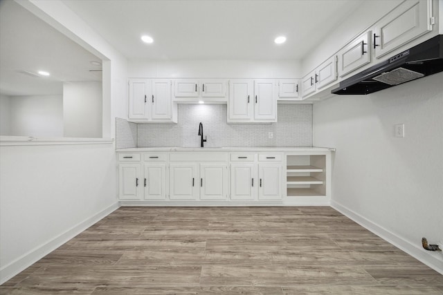 kitchen with decorative backsplash, white cabinetry, sink, and light wood-type flooring