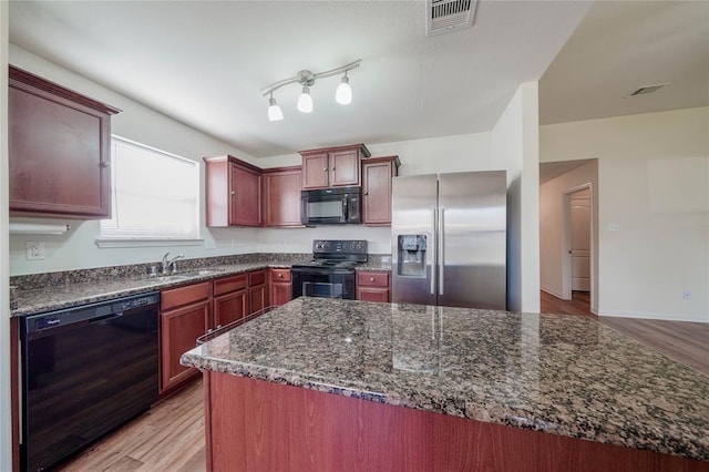 kitchen with dark stone countertops, sink, black appliances, and light wood-type flooring