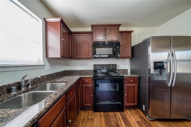 kitchen featuring black appliances, light hardwood / wood-style floors, dark stone countertops, and sink