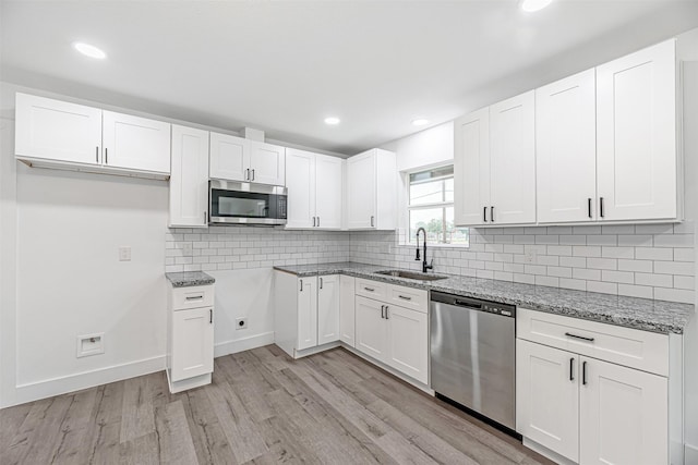 kitchen featuring stainless steel appliances, white cabinets, stone countertops, light hardwood / wood-style flooring, and sink