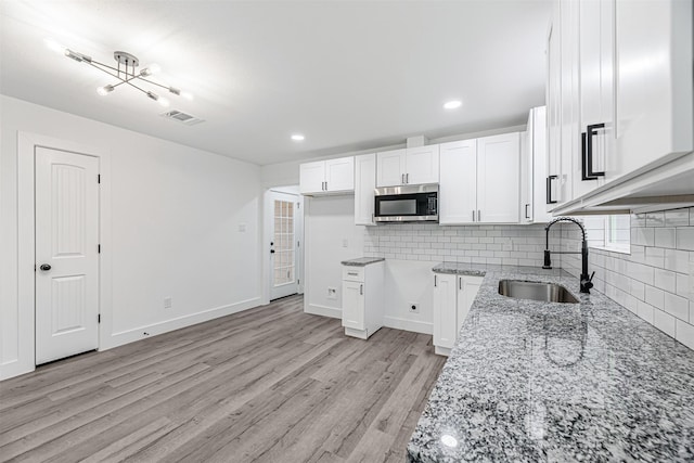 kitchen with light hardwood / wood-style floors, tasteful backsplash, white cabinets, light stone counters, and sink