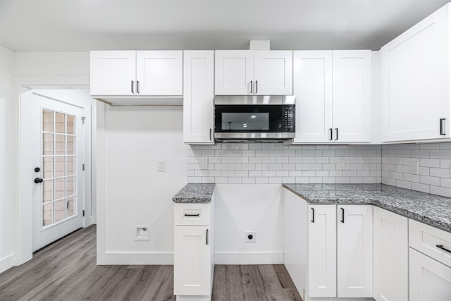 kitchen with white cabinets, light wood-type flooring, and dark stone countertops