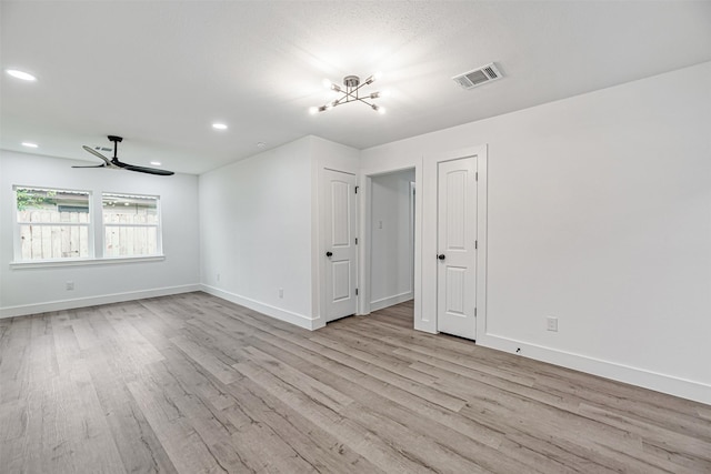 empty room featuring ceiling fan with notable chandelier and light hardwood / wood-style floors