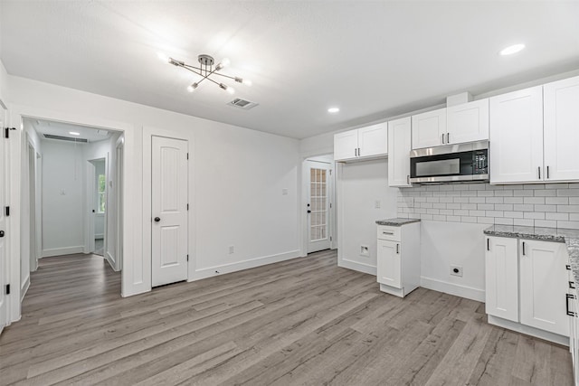 kitchen featuring white cabinetry, tasteful backsplash, stone countertops, a notable chandelier, and light wood-type flooring