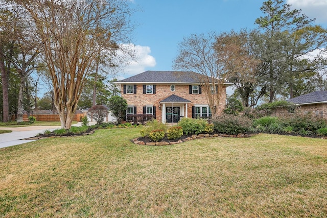 colonial-style house with brick siding, concrete driveway, a front yard, and fence