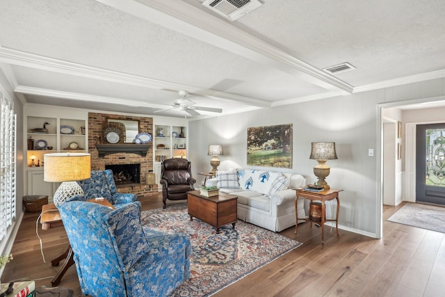 living room with a textured ceiling, ornamental molding, wood-type flooring, and built in shelves