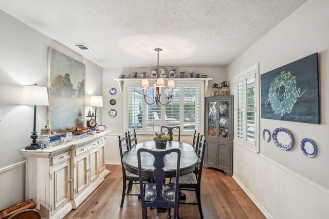 dining space with a textured ceiling, light hardwood / wood-style flooring, and a notable chandelier