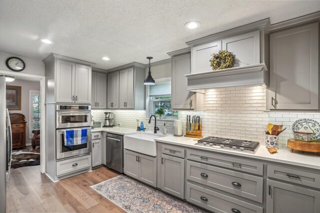 kitchen featuring pendant lighting, stainless steel appliances, sink, backsplash, and gray cabinetry