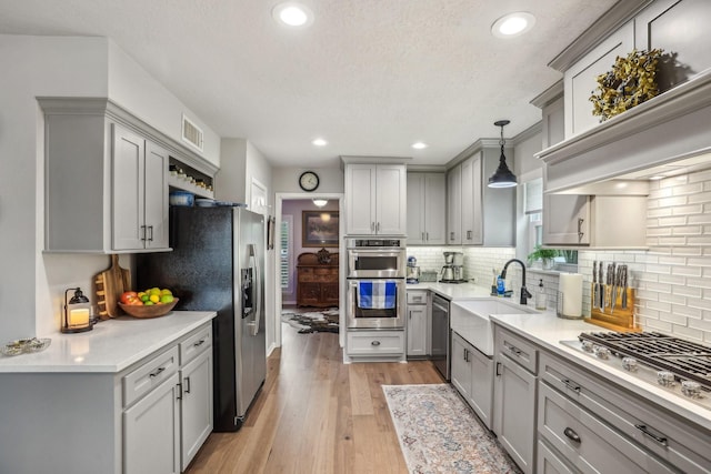 kitchen with decorative light fixtures, gray cabinetry, stainless steel appliances, tasteful backsplash, and light hardwood / wood-style flooring