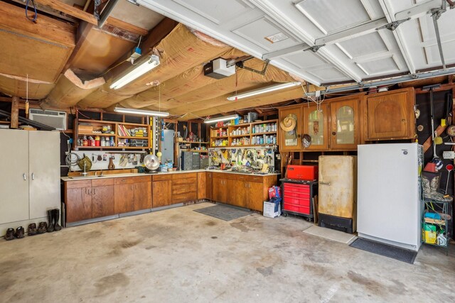 garage with a garage door opener, white refrigerator, a wall mounted AC, and a workshop area