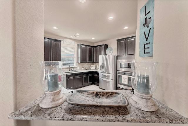 kitchen with light stone countertops, appliances with stainless steel finishes, decorative backsplash, and sink