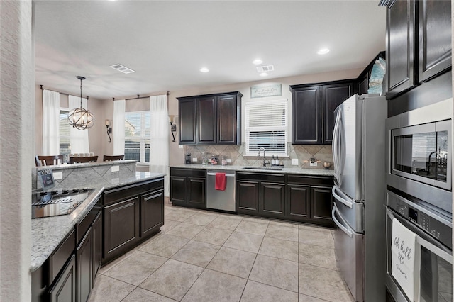 kitchen featuring light stone countertops, stainless steel appliances, a notable chandelier, hanging light fixtures, and light tile patterned flooring