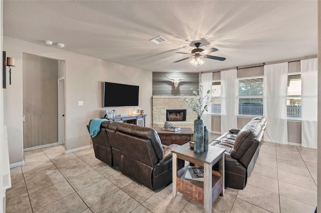 living room featuring ceiling fan, light tile patterned flooring, a stone fireplace, and a textured ceiling