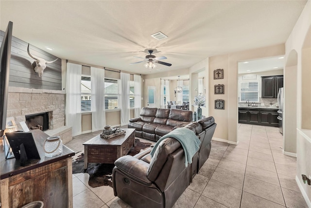 living room featuring a stone fireplace, ceiling fan, sink, and light tile patterned floors