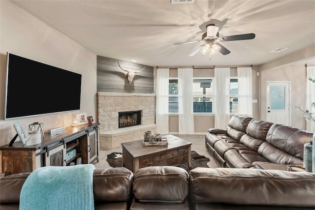 living room with a stone fireplace, wooden walls, and ceiling fan