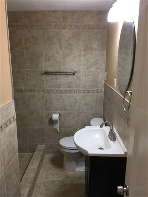 bathroom featuring tile patterned floors, a shower, toilet, vanity, and tile walls