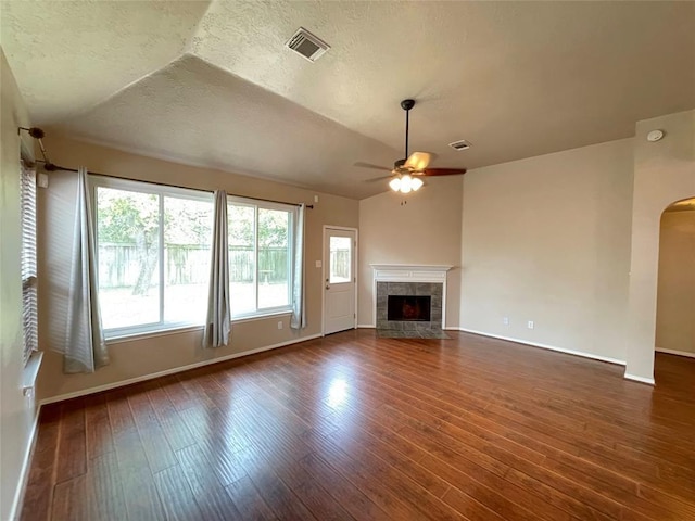 unfurnished living room with dark hardwood / wood-style floors, vaulted ceiling, ceiling fan, and a tiled fireplace