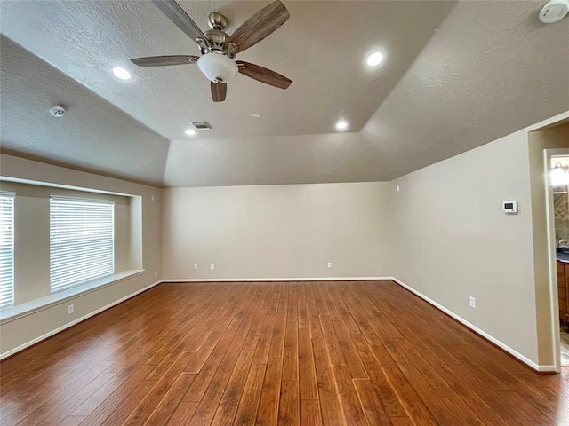 empty room with a textured ceiling, a tray ceiling, ceiling fan, hardwood / wood-style floors, and lofted ceiling