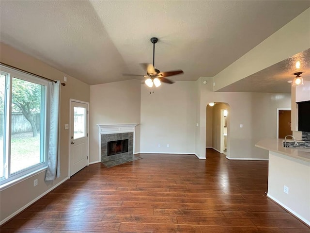 unfurnished living room with a tile fireplace, ceiling fan, dark hardwood / wood-style floors, and vaulted ceiling