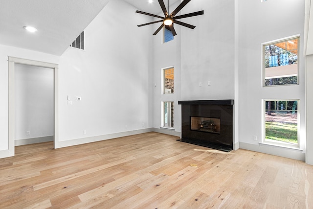 unfurnished living room with a high ceiling, light wood-type flooring, and ceiling fan