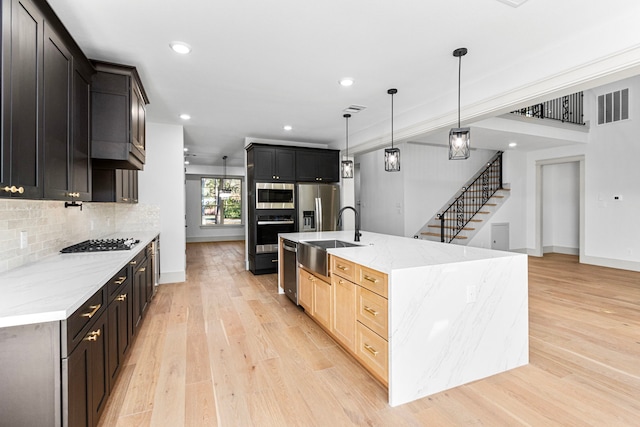 kitchen featuring decorative backsplash, appliances with stainless steel finishes, sink, pendant lighting, and light hardwood / wood-style floors