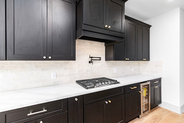 kitchen with stainless steel gas stovetop, backsplash, wine cooler, light hardwood / wood-style floors, and light stone counters