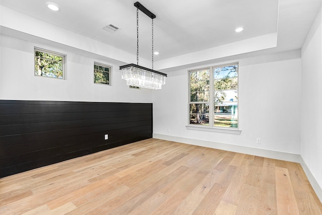 unfurnished dining area with a notable chandelier, a tray ceiling, and light hardwood / wood-style flooring