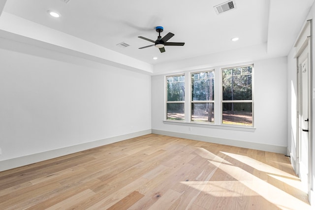 empty room featuring light wood-type flooring, a raised ceiling, and ceiling fan