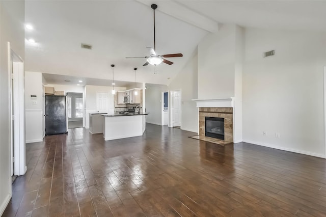 unfurnished living room with high vaulted ceiling, dark hardwood / wood-style flooring, a tiled fireplace, ceiling fan, and beam ceiling