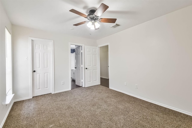 unfurnished bedroom with ceiling fan, ensuite bath, and dark colored carpet