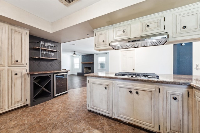 kitchen with ceiling fan, cream cabinets, a brick fireplace, beverage cooler, and stainless steel gas cooktop