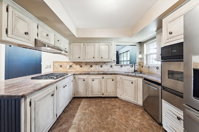 kitchen with light stone countertops, decorative backsplash, sink, stainless steel appliances, and a tray ceiling